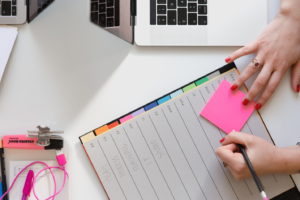 A person writing on a sticky note and a register