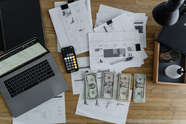 A computer, some documents, and money on a table.