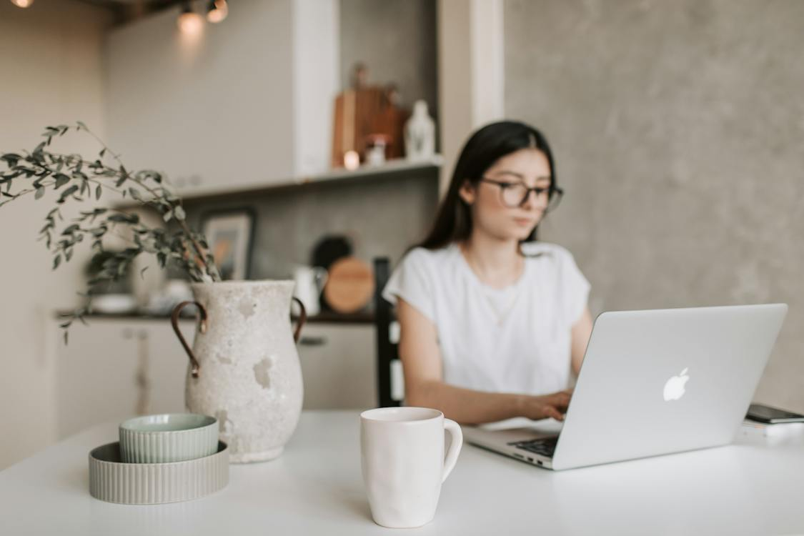 A mug in the foreground with a person using a laptop in the background