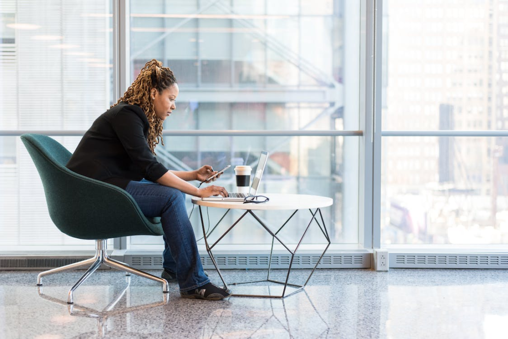 A person working on a laptop and holding a phone