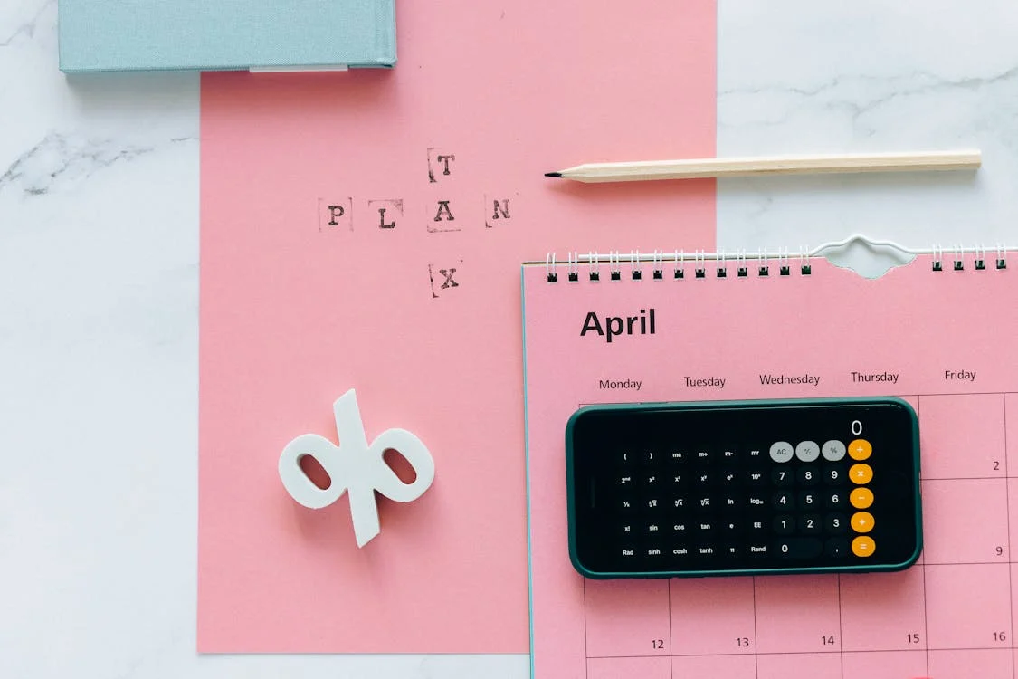 A pink planner alongside a smartphone displaying a calculator app.
