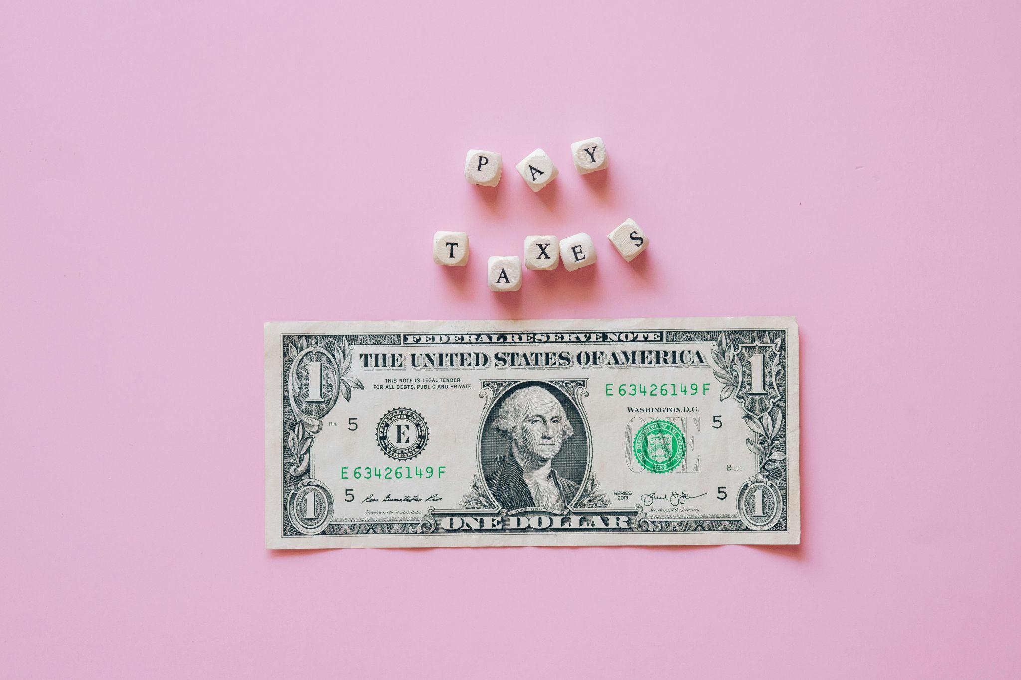Image of letter cubes spelling TAXES set against a pink background.