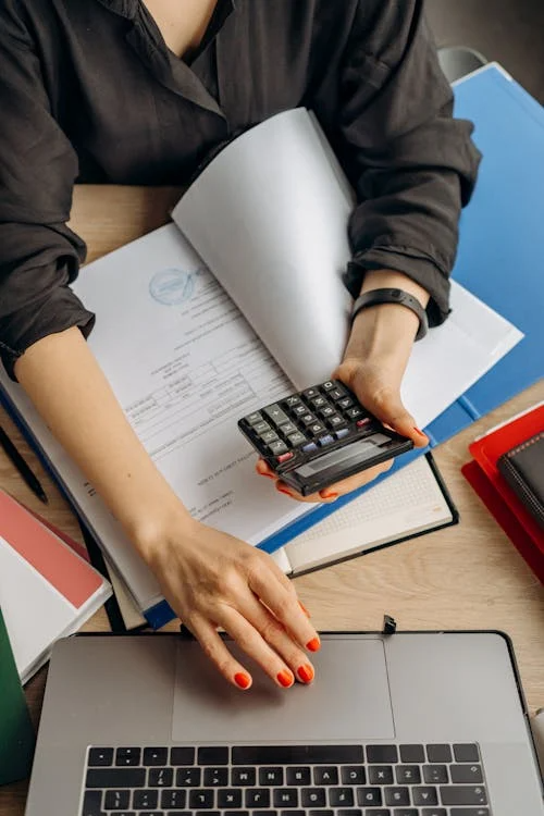 a woman wearing red nail polish holding a calculator and working on a laptop