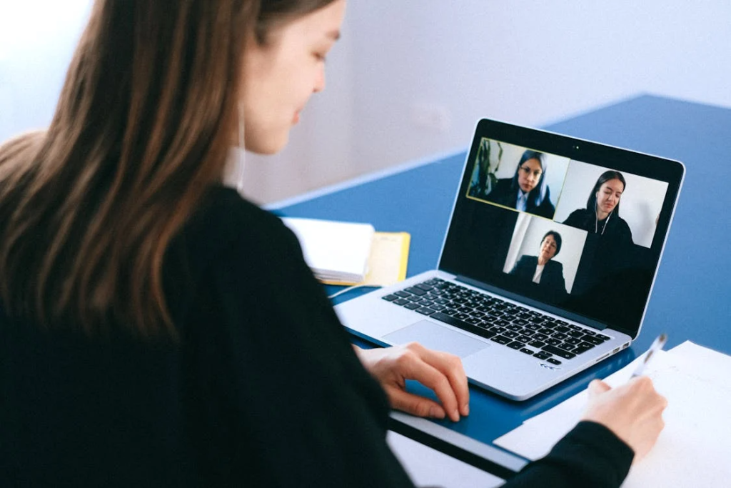 a woman writing down notes on paper while attending a webinar on her laptop in a black suit
