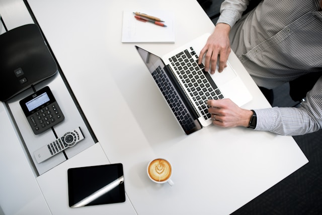 This photo shows a man working at desk with laptop, notebook and calculator