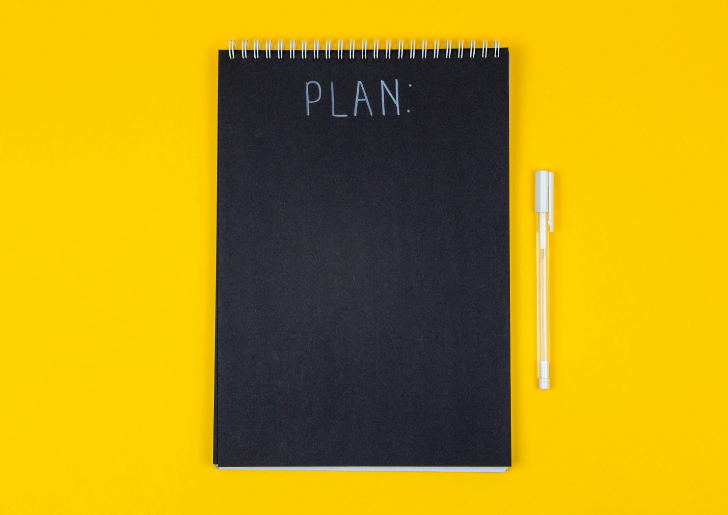 Black notebook with “PLAN” written on top with a white pen next to it