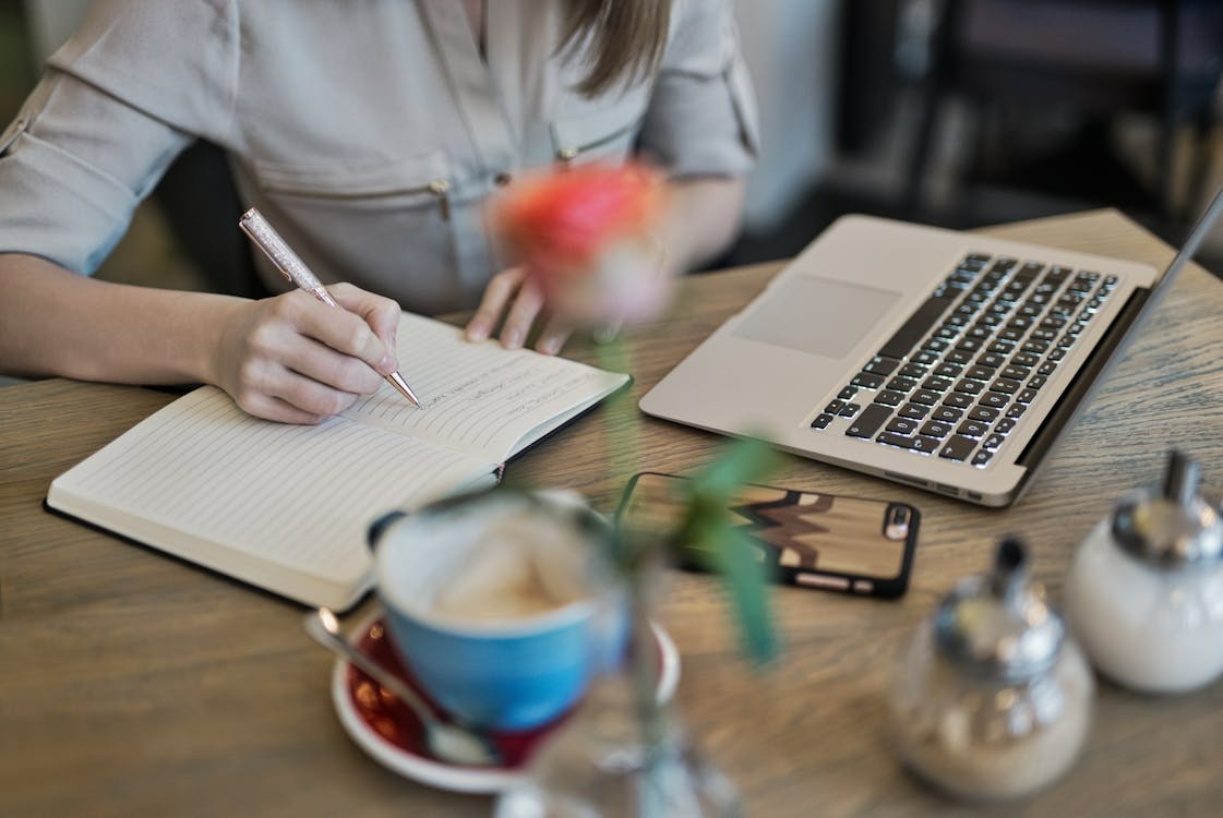 Woman writing notes beside a laptop on a desk