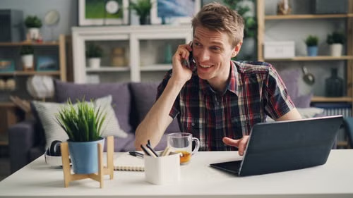 A smiling man talking on a phone while working remotely from home