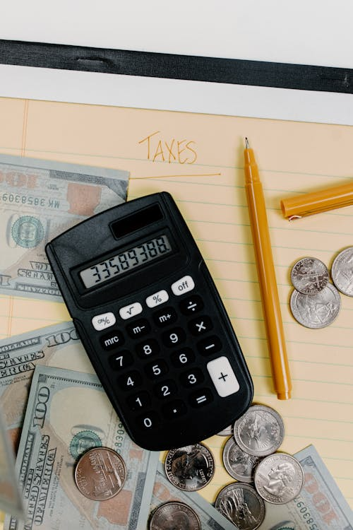 A calculator, coins, and US dollars on top of a paper with Taxes written on it