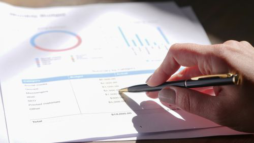 Hand holding a pen over a printed business expense report with financial charts
