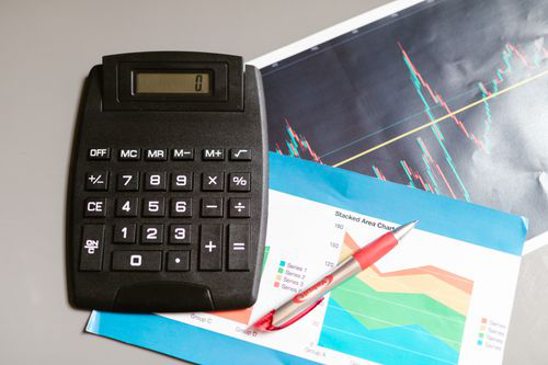 Calculator and pen placed on printed business charts and financial reports