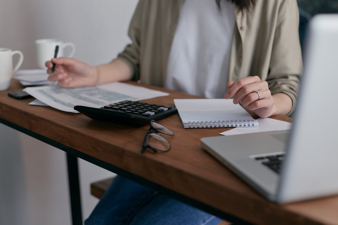 A bookkeeping consultant holding a pen while working on tax documents using a laptop and calculator
